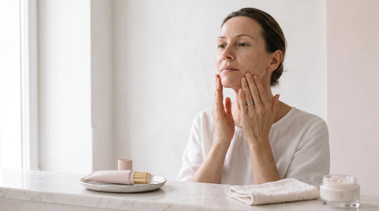 Mujer madura aplicando crema facial reafirmante sobre la línea mandibular en un baño luminoso